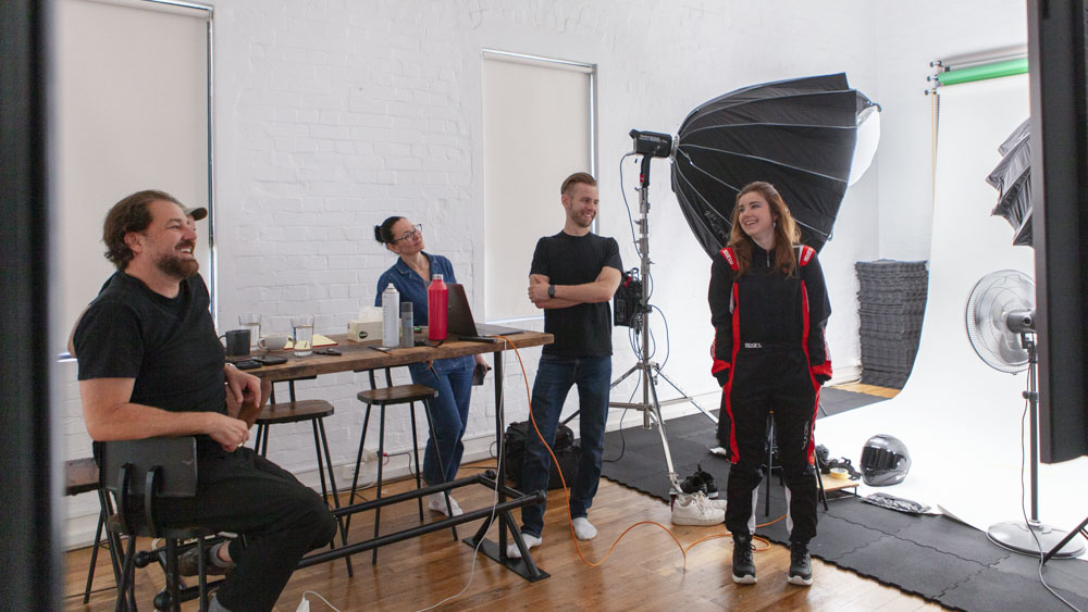 Behind the scenes at a lively photo shoot with cheerful crew members and a professional setup, shot at The Signal Box studio with lighting setup.