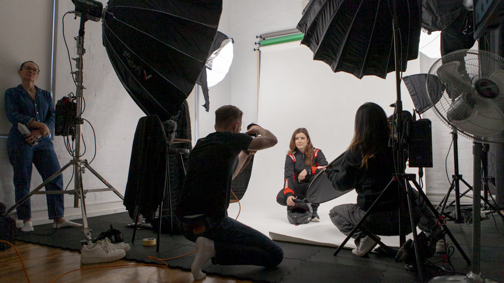 A behind-the-scenes glimpse of a studio photoshoot in action, with a photographer capturing images of a seated woman while assistants and lighting equipment surround them, highlighting the collaborative effort that goes into professional photography.