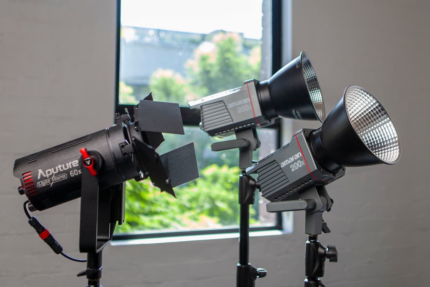 Three professional studio lights on stands ready for a photoshoot or video recording session, with a window providing natural light in the background.